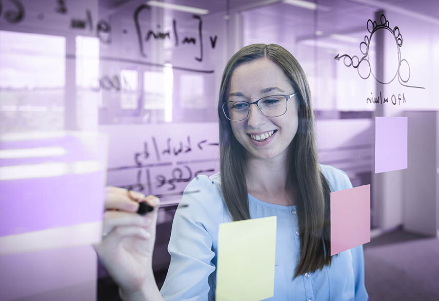  Young woman student writes on glass board | Sandler Group 