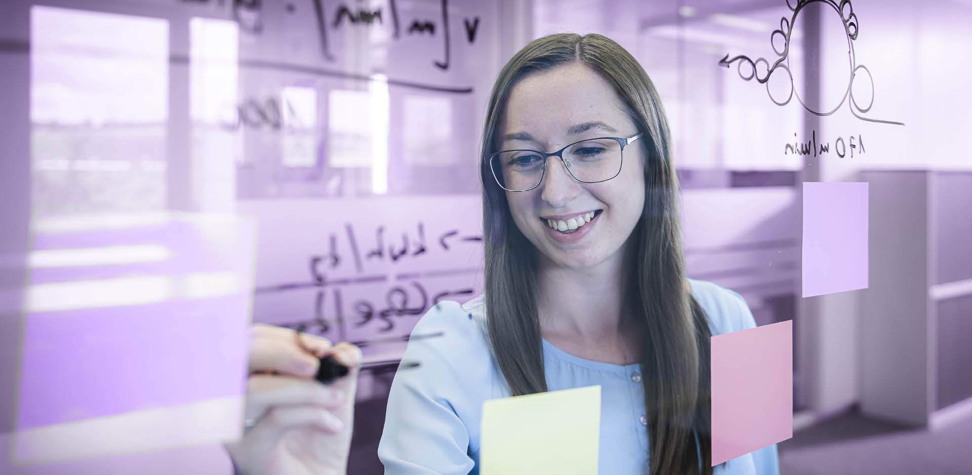 Young woman student writes on glass board | Sandler Group 
